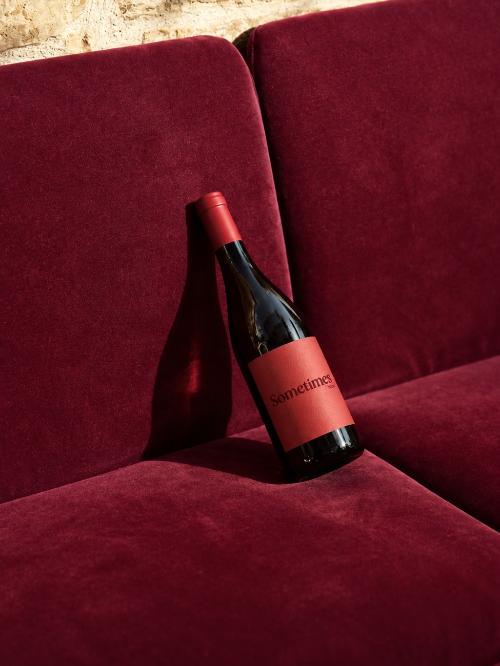 A bottle of Sometimes Wine resting on a deep red velvet banquette